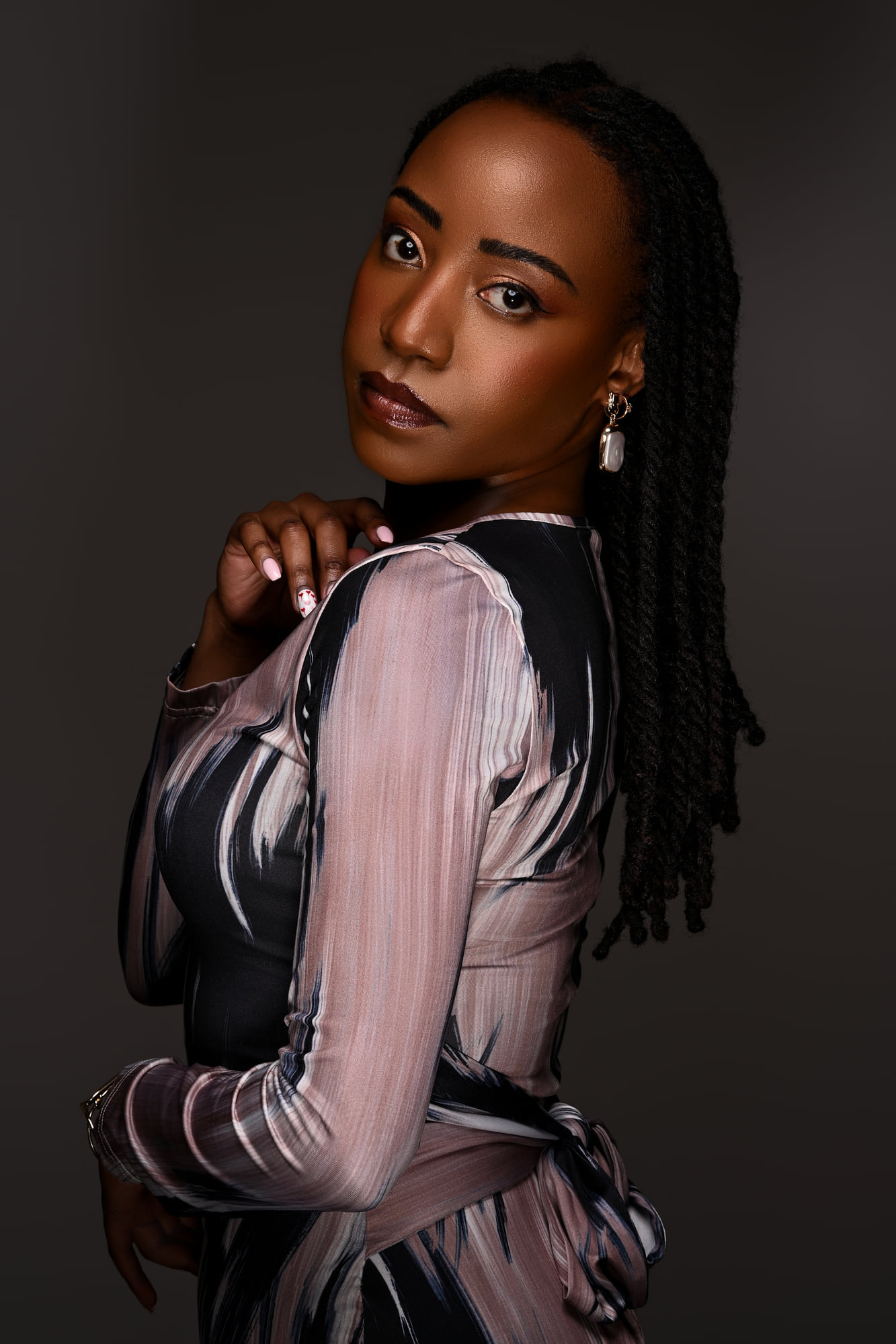 Lorna Ishimwe in a printed long-sleeved dress, close editorial portrait against a deep grey studio ground.