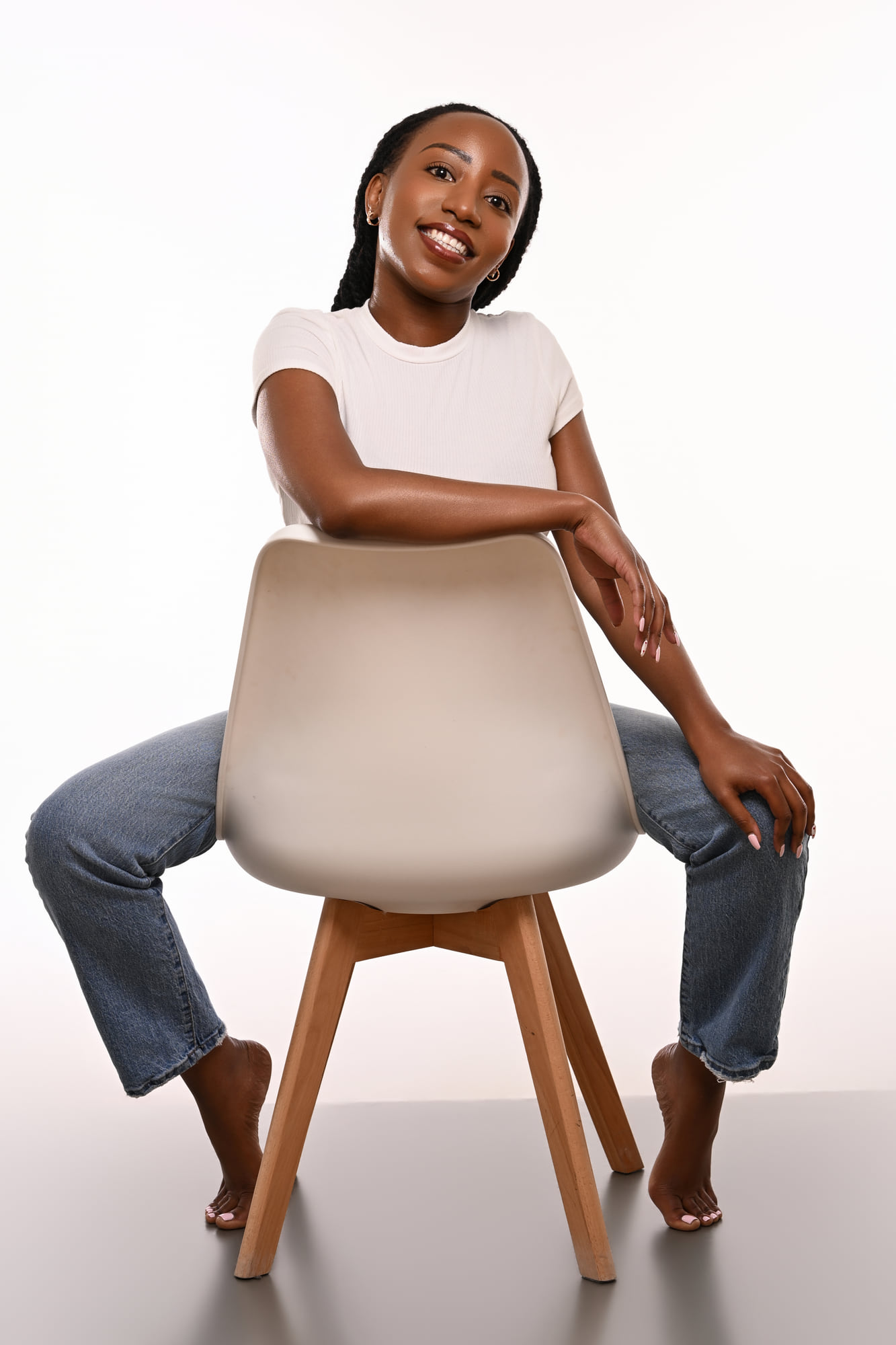Lorna Ishimwe seated on a studio chair in a white t-shirt and denim.