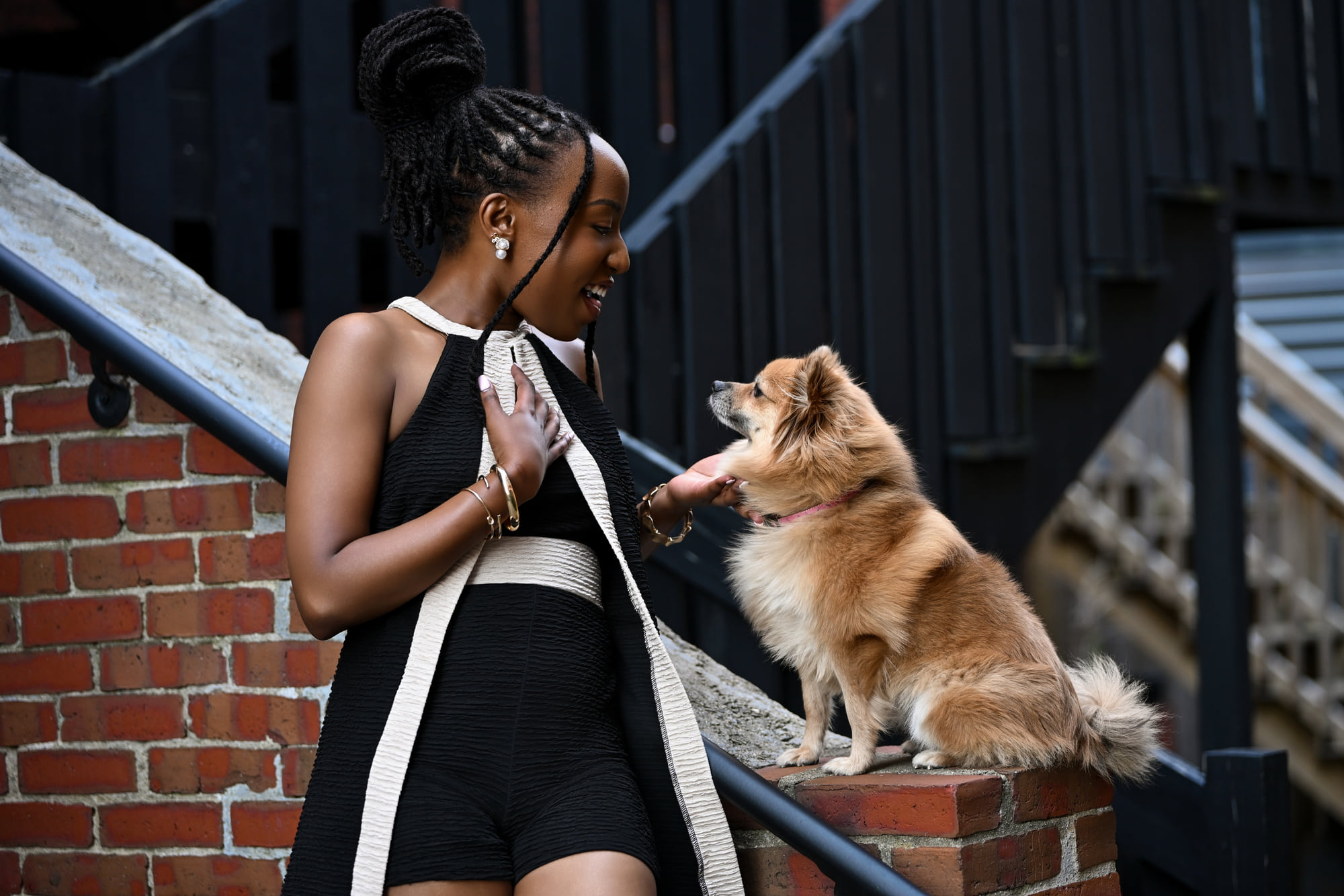 Lorna Ishimwe on location in a black and white outfit, greeting a small dog on a city street.
