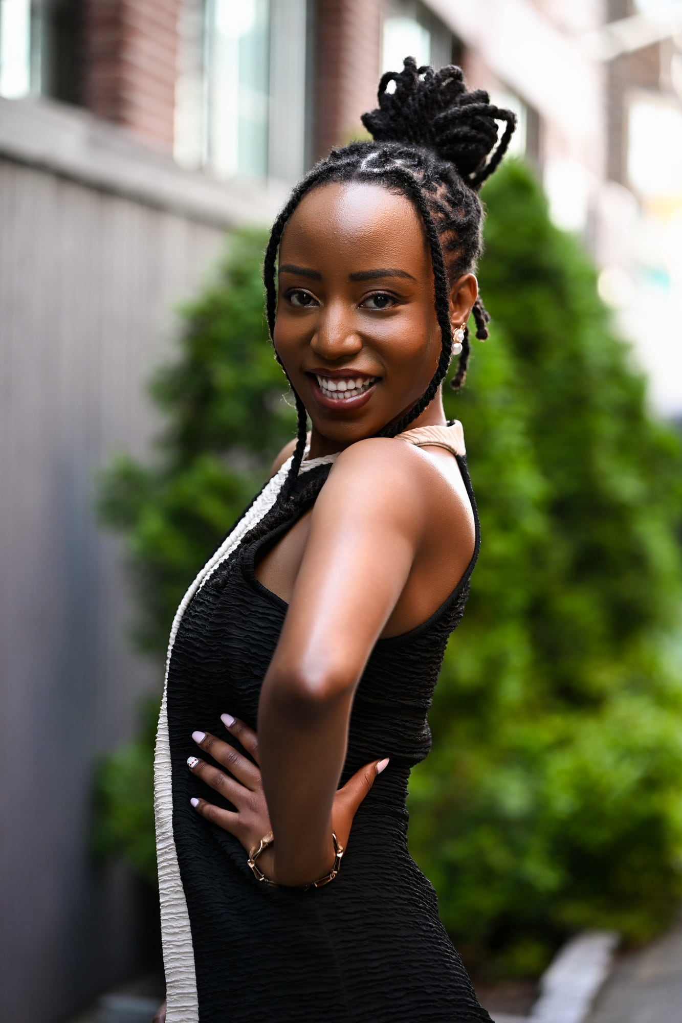 Lorna Ishimwe on location in a black sleeveless outfit beside garden greenery.